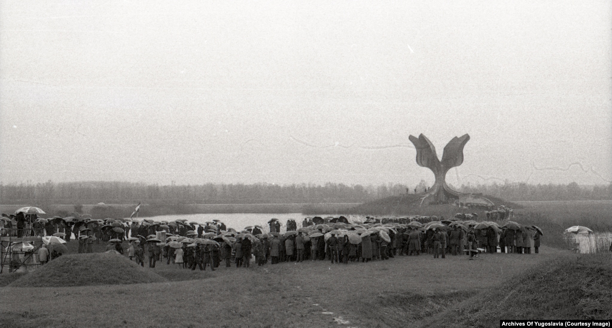 Eine große Menschenmenge mit Regenschirmen im Regen vor der Jasenovac-Gedenkblume, 1980.